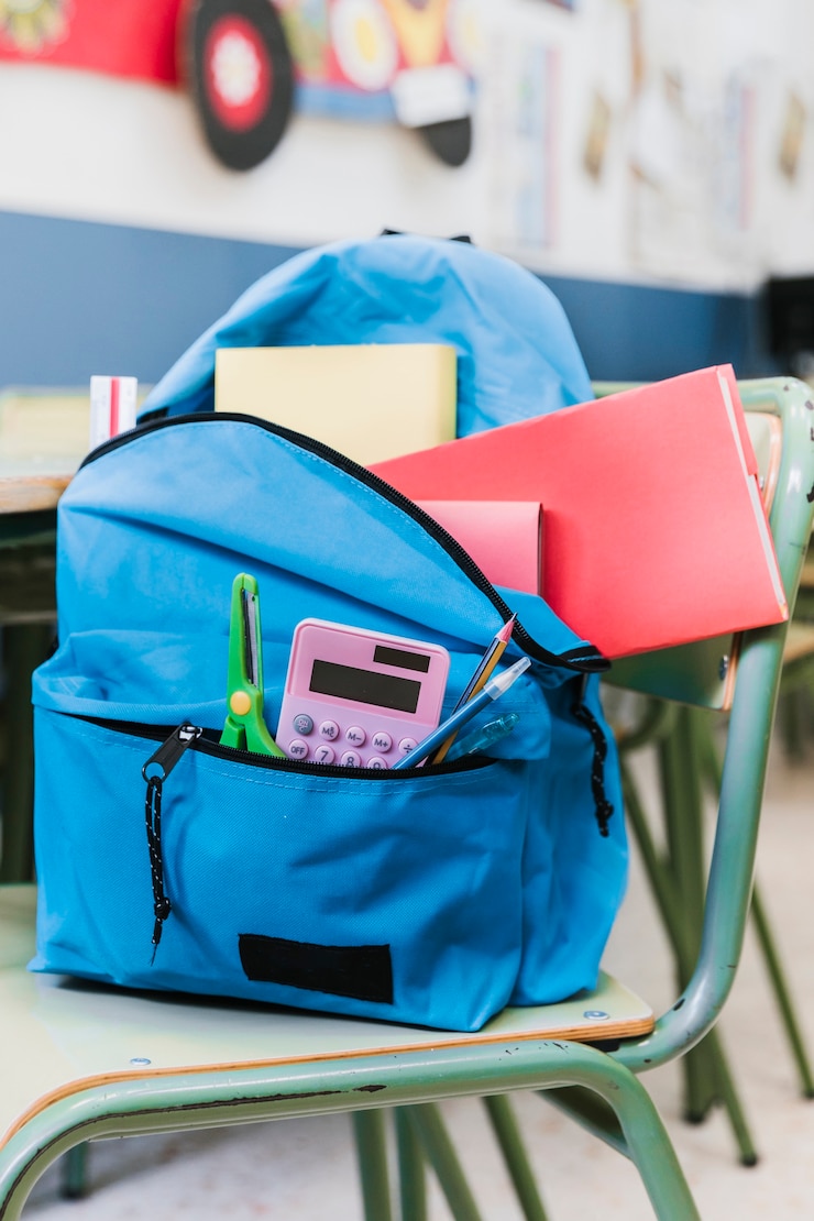 Foto gratuito mochila con papelería en silla.