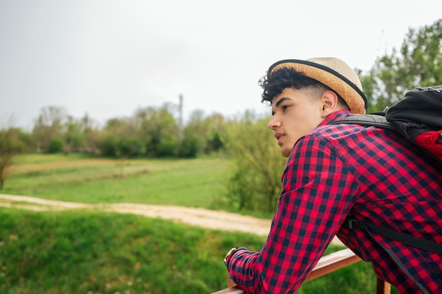 Foto gratuita mochila que lleva del sombrero del hombre que lleva joven que mira lejos