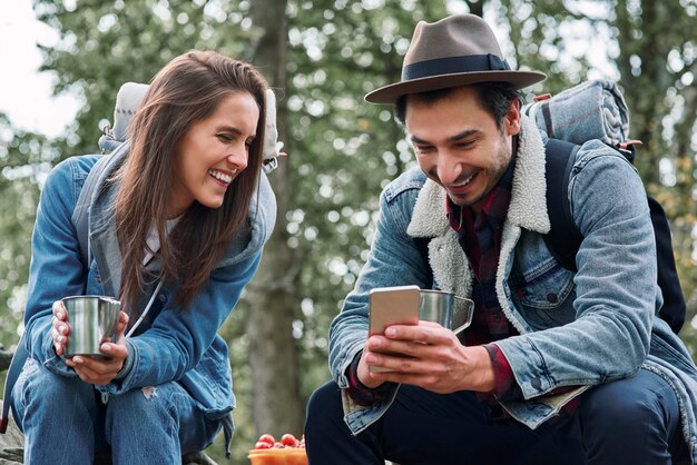 Mochileros felices tomando café y usando teléfono móvil