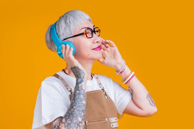 Moda asiática senior anciana mujer usar auriculares escuchando música melodía mientras usa delantal mano toque auricular casual relajarse estilo de vida fácil escuchar música asia mujer con tatuaje cerca de los ojos siéntase libre