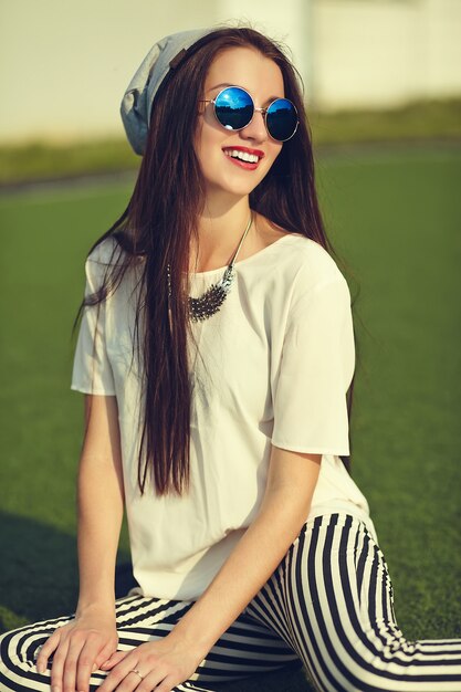 moda elegante hermosa morena joven modelo en ropa casual de verano hipster posando en el fondo de la calle en el parque