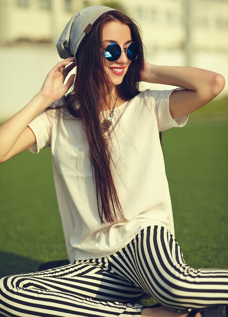 moda elegante hermosa morena joven modelo en ropa casual de verano hipster posando en el fondo de la calle en el parque