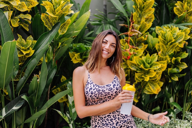 Moda elegante joven caucásica ajuste mujer deportiva en leopardo cami top y pantalones cortos de motociclista fuera tiene coctelera de proteínas