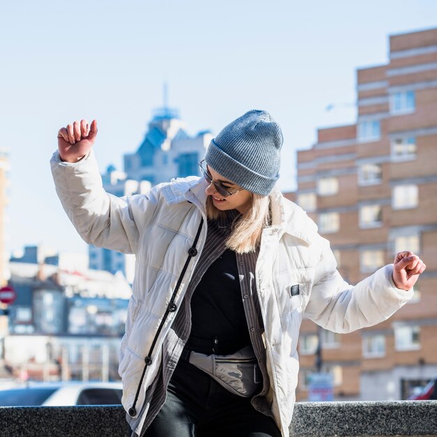 Moda joven con sombrero de punto azul bailando en la ciudad