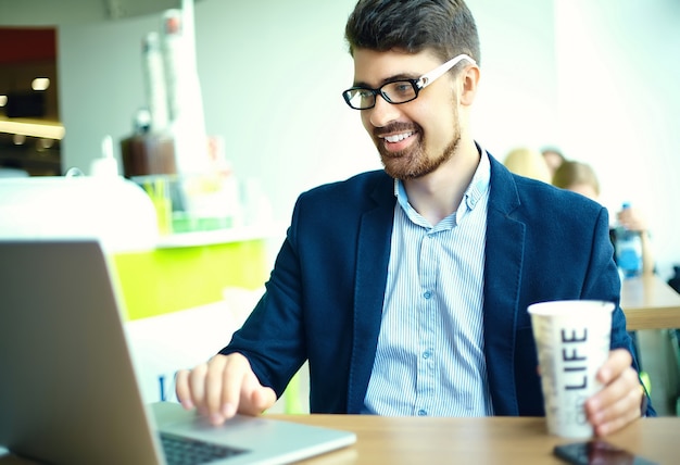 Moda joven sonriente hipster hombre tomando café en la cafetería de la ciudad durante la hora del almuerzo con cuaderno en traje