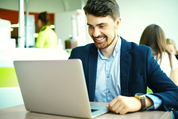 Moda joven sonriente hombre hipster en el café de la ciudad durante la hora del almuerzo con cuaderno en traje