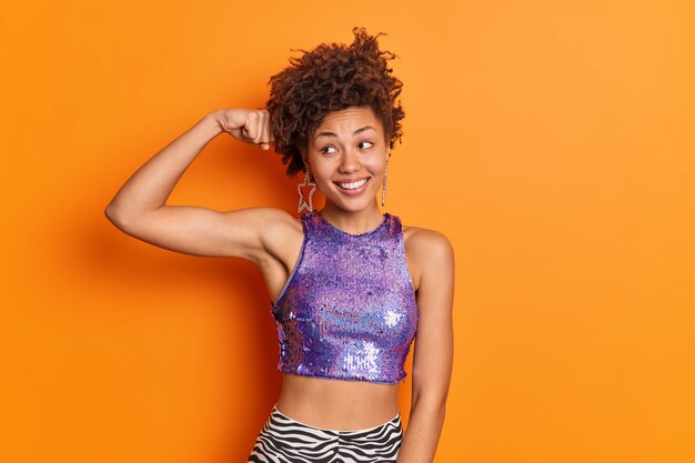 Moda mujer afroamericana de piel oscura con cabello rizado levanta el brazo y muestra los músculos