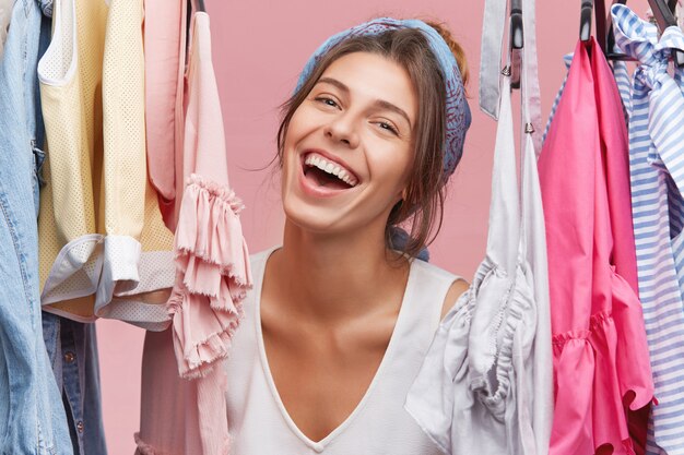 Moda mujer elegir vestido en fecha o fiesta, sintiéndose emocionado y feliz. Mujer alegre que mira complacida mientras empaca la bolsa antes del viaje, de pie en su armario con bastidores llenos de ropa