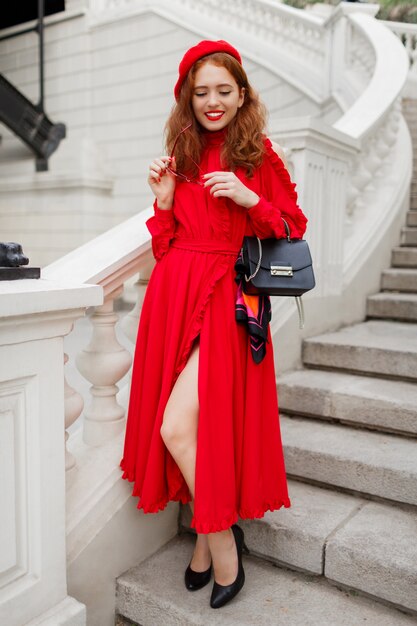 moda mujer jengibre en boina roja y elegante vestido posando al aire libre.