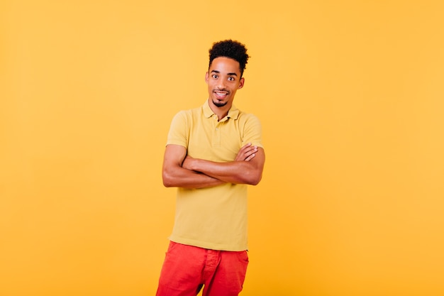 Modelo africano bien vestido sorprendido que presenta con los brazos cruzados. Filmación en interiores del hombre asombrado de pie en pose de confianza.