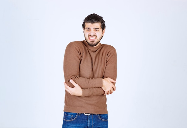 modelo atractivo joven en suéter marrón haciendo gestos sobre la pared blanca.