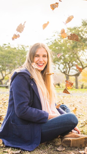 Modelo atractivo sentado en el suelo de otoño y sonriendo a la cámara