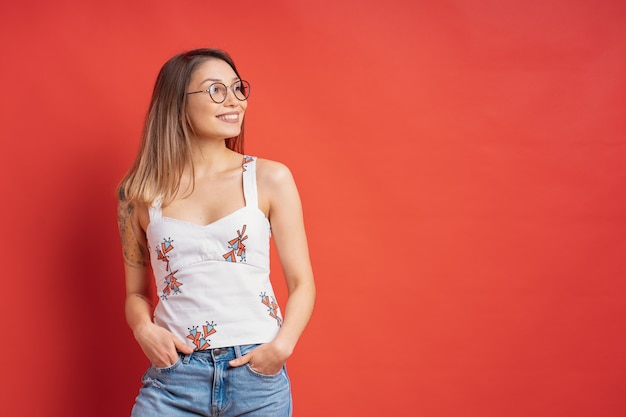 Modelo bastante femenino posando con una expresión de la cara sonriente en la pared roja