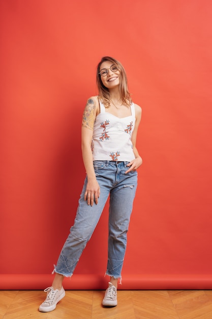 Modelo bastante femenino posando con una expresión de la cara sonriente en la pared roja