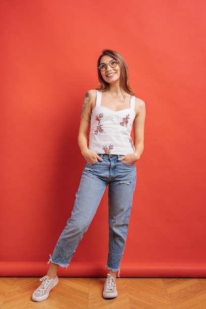 Modelo bastante femenino posando con una expresión de la cara sonriente en la pared roja