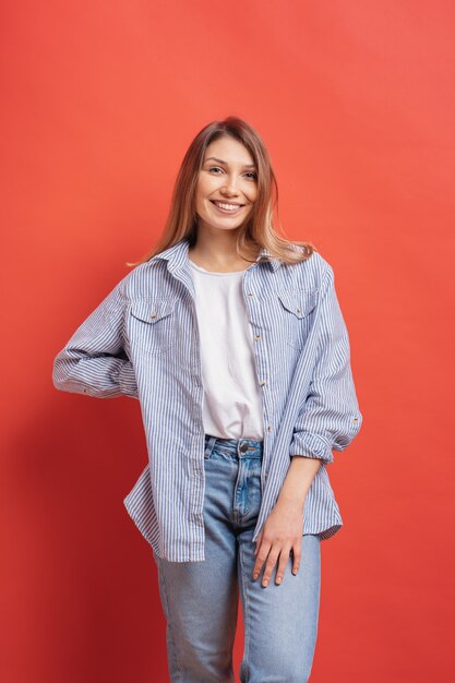 Modelo bastante femenino posando con una expresión de la cara sonriente en la pared roja