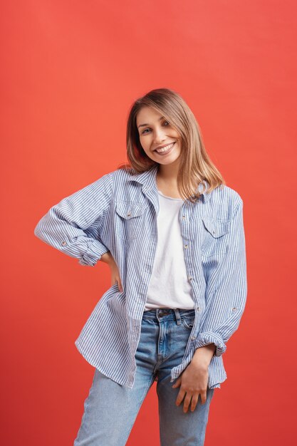 Modelo bastante femenino posando con una expresión de la cara sonriente en la pared roja