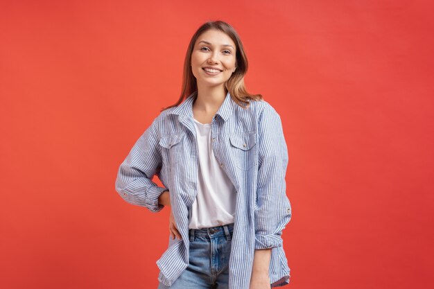 Modelo bastante femenino posando con una expresión de la cara sonriente en la pared roja