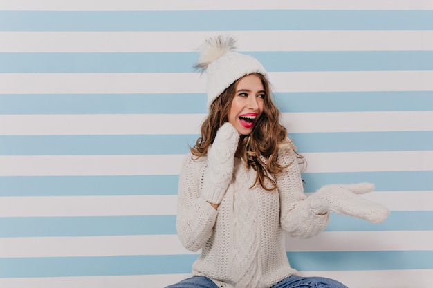 Foto gratuita modelo blanco astuto, divertido, juguetonamente con risa mirando a la derecha retrato de mujer sentada en el suelo con ropa de invierno en interiores