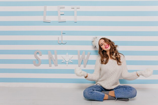 Modelo blanco travieso fantástico divirtiéndose sentado. Mujer joven se ríe y posa sobre la inscripción "Let it snow"