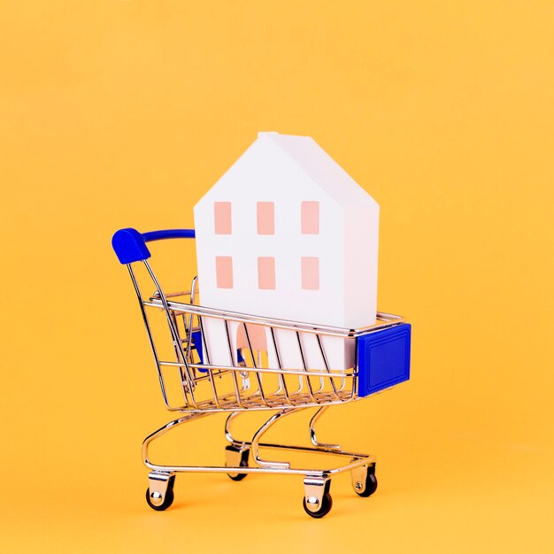 Modelo de casa dentro de la cesta de compras con fondo amarillo