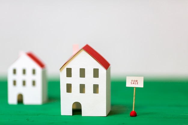 Modelo de casa en miniatura cerca de la etiqueta de venta en el escritorio con textura verde sobre fondo blanco