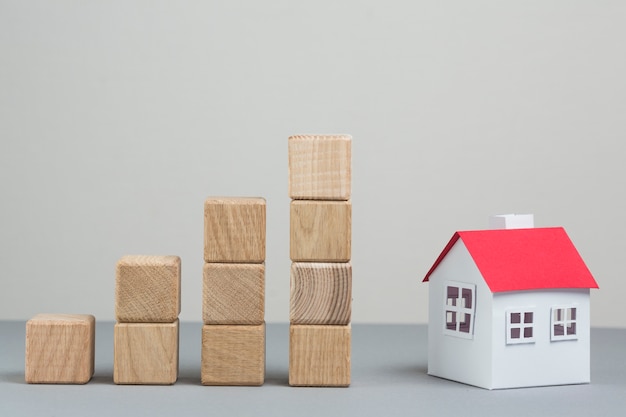 Modelo de casa pequeña y pila de bloques de madera en aumento sobre fondo gris