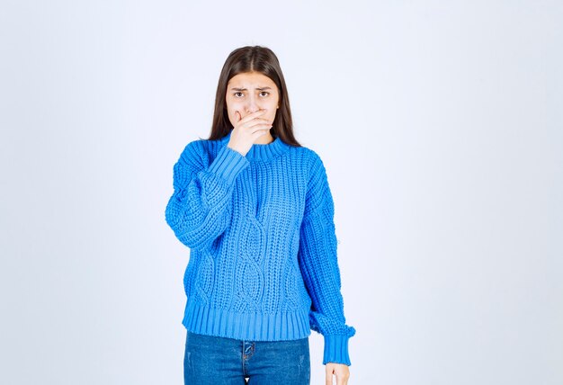 modelo de chica joven en suéter azul coning boca con una mano en blanco-gris.