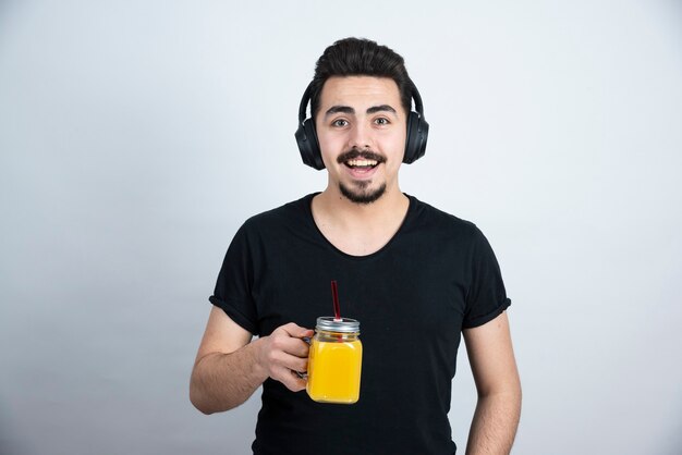 modelo de chico guapo en auriculares sosteniendo un vaso con jugo de naranja.