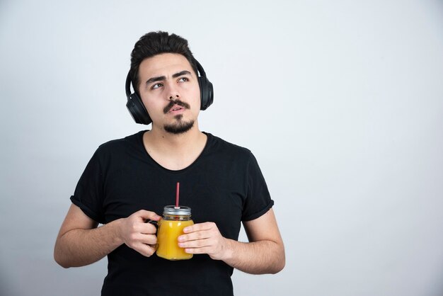 modelo de chico guapo en auriculares sosteniendo un vaso con jugo de naranja.