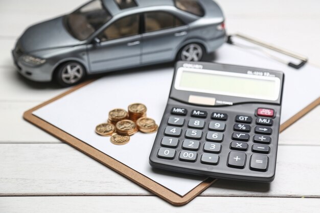 Modelo de coche, calculadora y monedas en la mesa blanca
