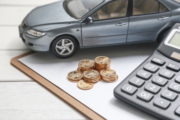 Modelo de coche, calculadora y monedas en la mesa blanca