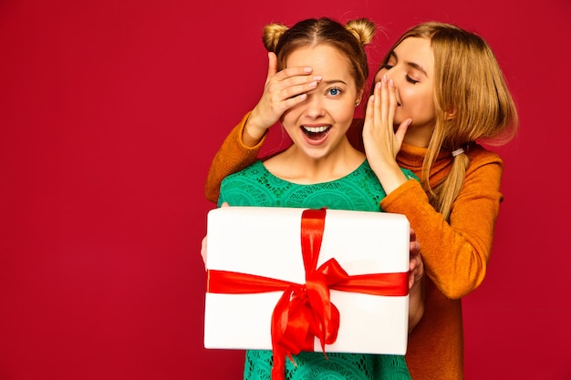 Modelo cubriendo los ojos de su amiga y dándole una gran caja de regalo y un secreto secreto