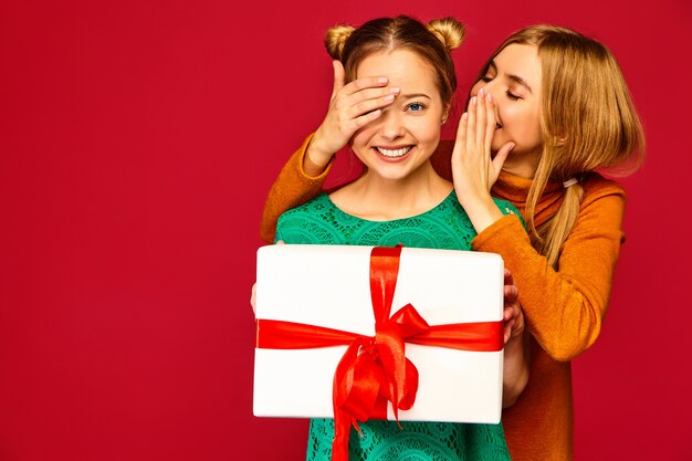 Modelo cubriendo los ojos de su amiga y dándole una gran caja de regalo y un secreto secreto