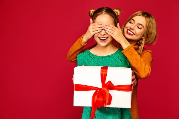 Modelo cubriéndole los ojos a su amiga y dándole una gran caja de regalo