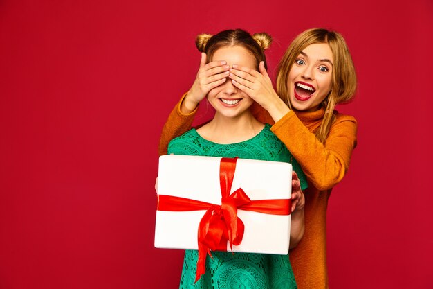 Modelo cubriéndole los ojos a su amiga y dándole una gran caja de regalo