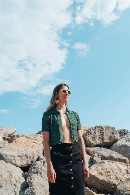 Modelo elegante en chaqueta verde con anteojos de pie contra rocas apiladas