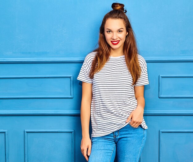 Modelo elegante joven en ropa casual de verano con labios rojos, posando junto a la pared azul