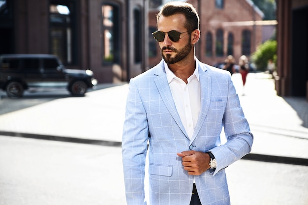 modelo de empresario de moda guapo vestido con elegante traje azul posando en la calle