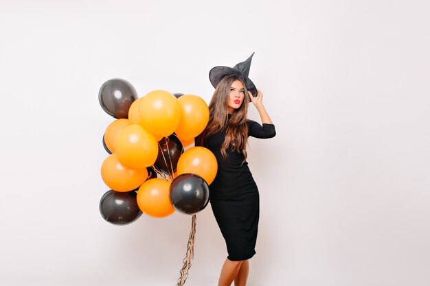 Modelo femenino bien proporcionado con sombrero de bruja sonriendo antes de la fiesta de halloween