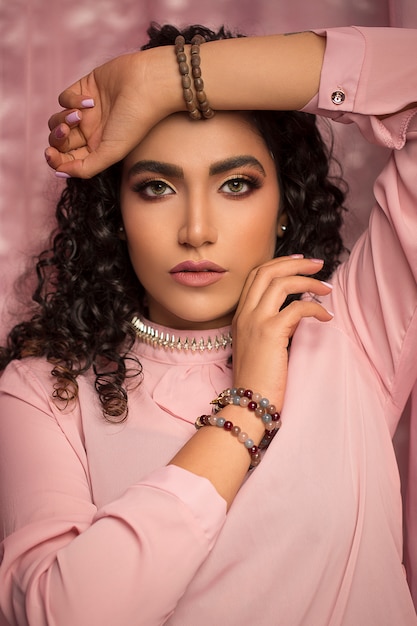 Modelo femenino en camisa casual rosa y maquillaje ligero con joyas boho