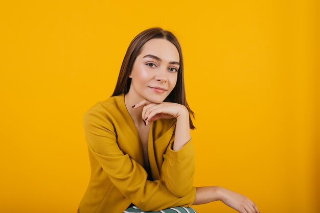 Modelo femenino en chaqueta amarilla de moda posando. Foto interior de mujer morena complacida con cabello oscuro posando