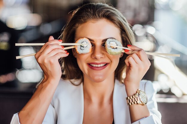 Modelo femenino de estilo de vida saludable sonriendo feliz sosteniendo palillos en los ojos.