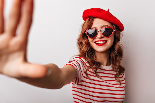 Modelo femenino francés despreocupado en la boina sonriente Chica emocional en accesorios casuales posando.