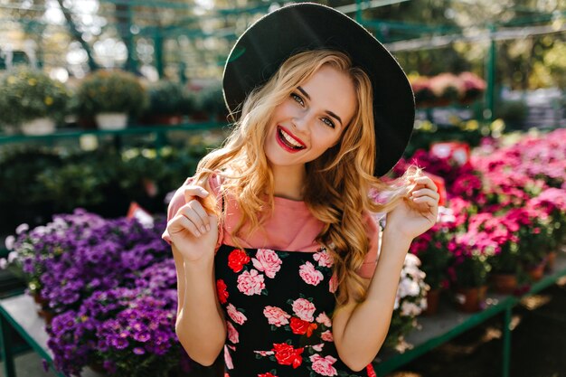 Modelo femenino inspirado en pie del sombrero en la franja de flores coloridas. Retrato de mujer atractiva ciega relajante en invernadero.