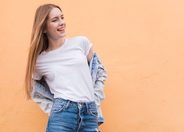 Modelo femenino joven sonriente que presenta en la pared beige texturizada