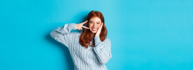Foto gratuita modelo femenino pelirroja alegre que envía buenas vibraciones sonriendo y mostrando el signo de la paz sobre azul b