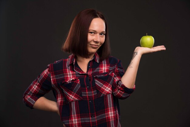 Modelo femenino en trajes de colección otoño invierno sosteniendo una manzana verde y apuntando a ella.