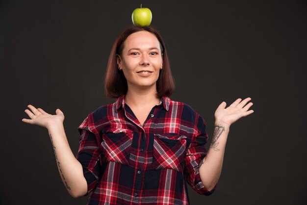 Modelo femenino en trajes de colección otoño invierno sosteniendo una manzana verde en la cabeza.