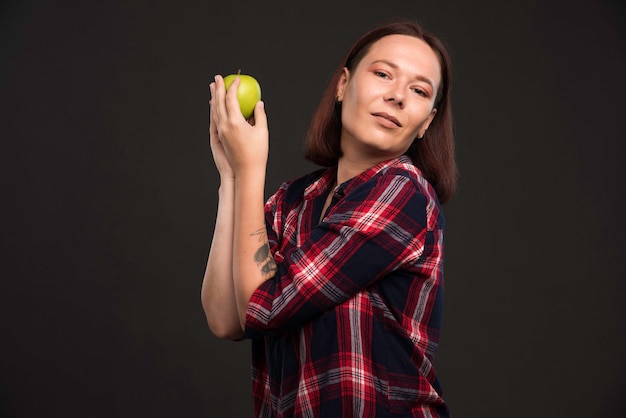 Modelo femenino en trajes de colección otoño invierno sosteniendo una manzana verde y disfrutándola.